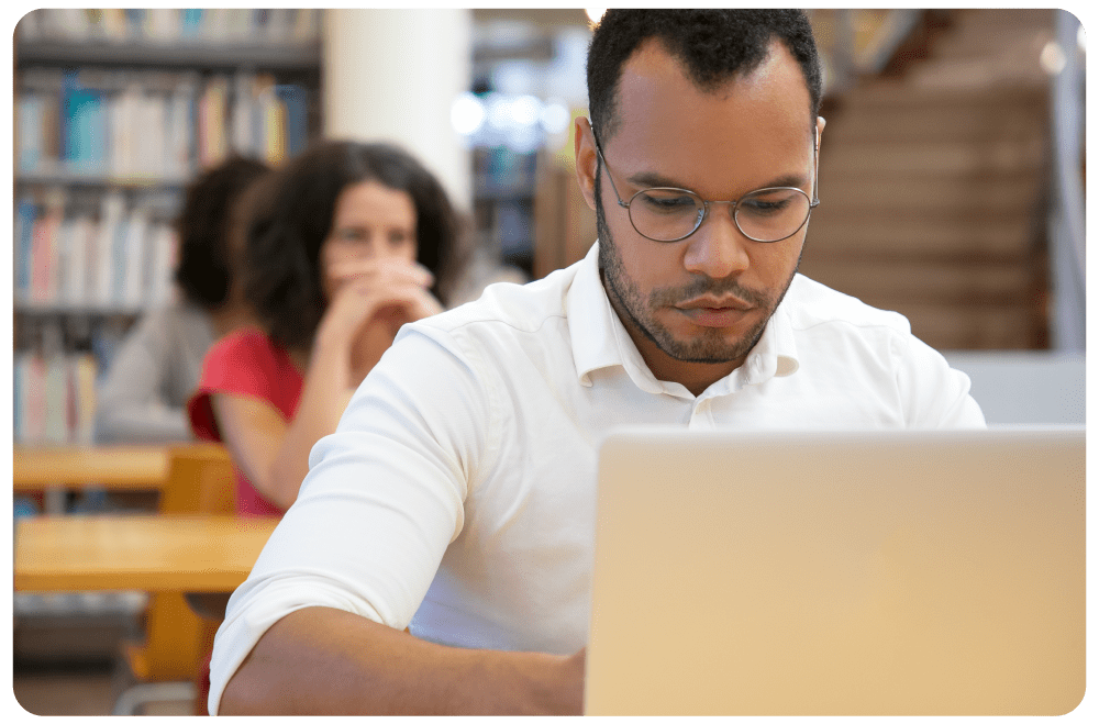 Cybersecurity Soft Start Student studying cybersecurity online using a laptop in a library setting, representing adult learners and working professionals pursuing beginner-friendly cybersecurity courses.
