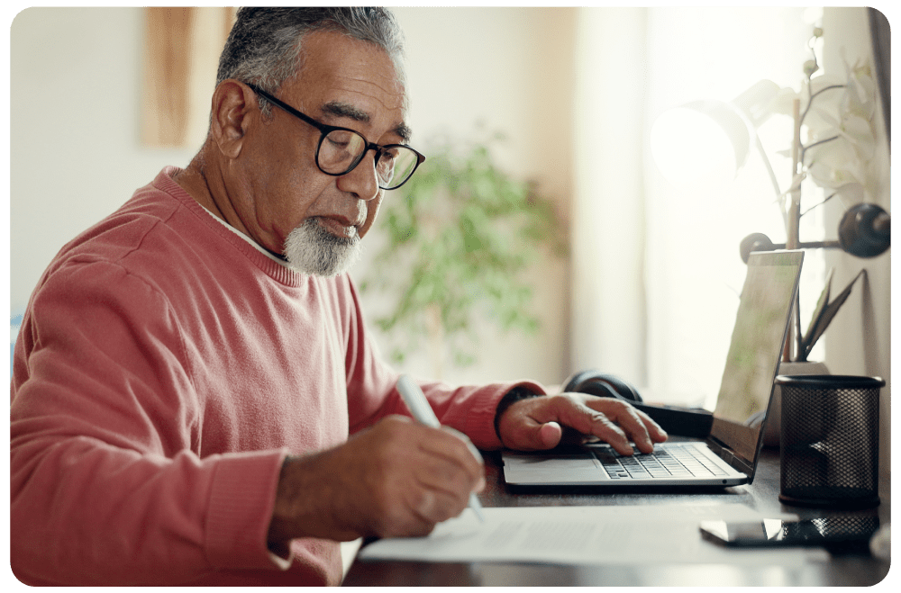 Cybersecurity Soft Start Adult learner studying from home, taking notes while completing an online cybersecurity course on a laptop.